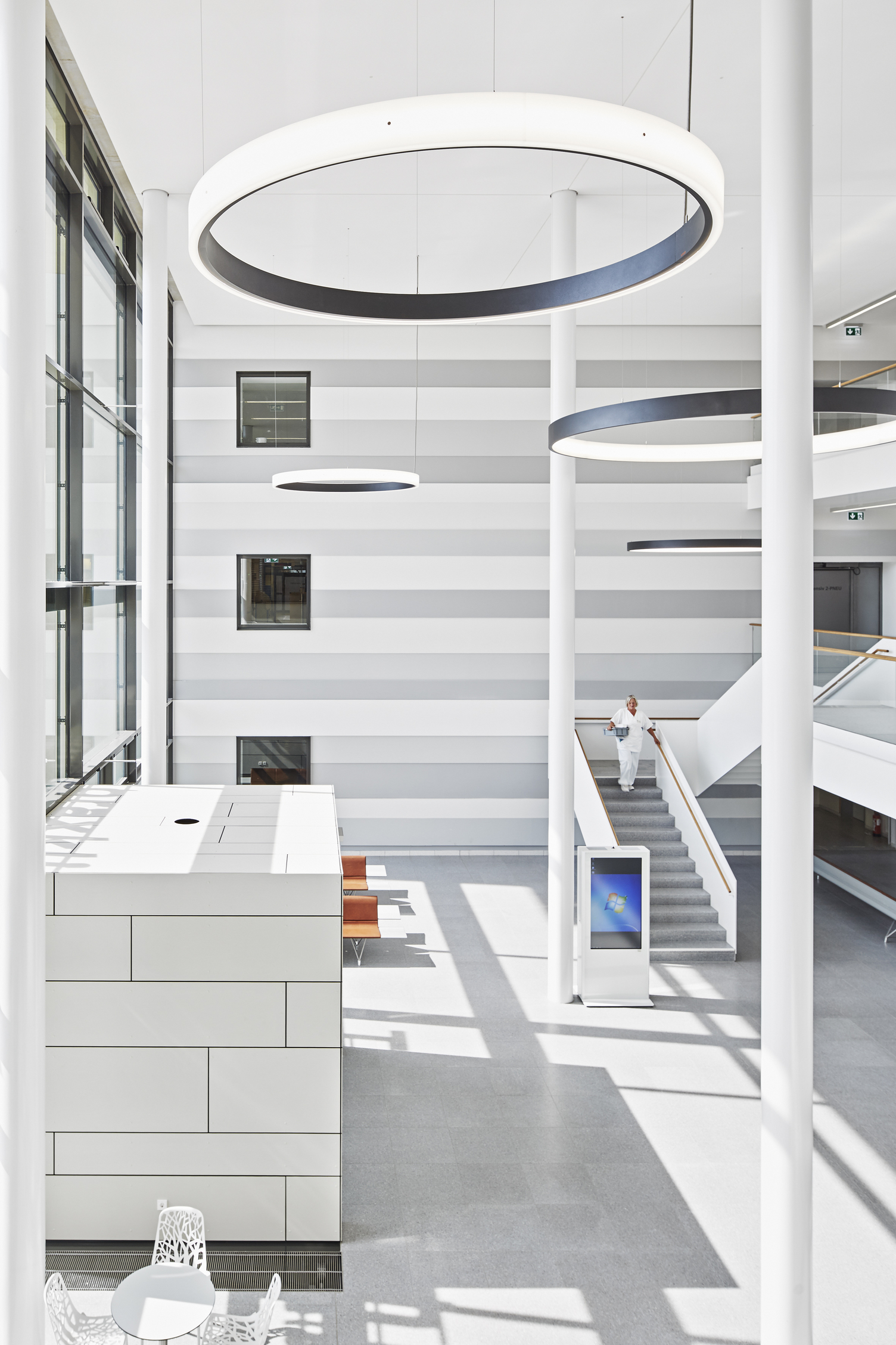 Eingangshalle & Treppenhaus Thoraxklinik mit CIRCOLO Ringleuchten | © Dietmar Strauß / Besigheim Hohe weiße Eingangshalle der Thoraxklinik mit Säulen, 2 große schwarze Ringleuchten nach innenstrahlend (CIRCOLO I) und 2 Ringleuchten (CIRCOLO INVERSE) nach außenstrahlend im Raum abgehangen, eine Person läuft die Treppe hinunter. | © Dietmar Strauß / Besigheim