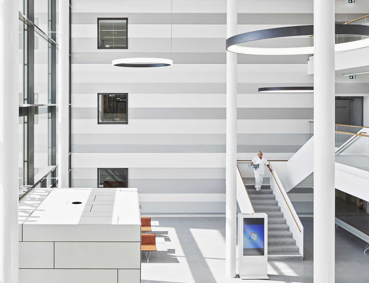 Eingangshalle & Treppenhaus Thoraxklinik mit CIRCOLO Ringleuchten Hohe weiße Eingangshalle der Thoraxklinik mit Säulen, 2 große schwarze Ringleuchten nach innenstrahlend (CIRCOLO I) und 2 Ringleuchten (CIRCOLO INVERSE) nach außenstrahlend im Raum abgehangen, eine Person läuft die Treppe hinunter.