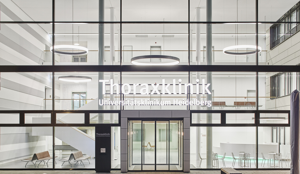 Eingangshalle & Treppenhaus Thoraxklinik mit CIRCOLO Ringleuchten Querbild: Außenansicht durch Glasfront auf Eingangshalle der Thoraxklinik mit Säulen und großen Ringleuchten abgehangen auf verschiedene Ebenen