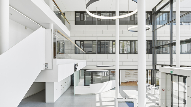 Landscape: High white entrance hall of the Thorax Clinic with a view of the reception desk, above which two round luminaires with acoustic foil are suspended to provide privacy, in the room columns and 2 large black ring luminaires radiating inwards (CIRCOLO I) and 2 ring luminaires (CIRCOLO INVERSE) suspended in the room radiating outwards. | © Dietmar Strauß / Besigheim
