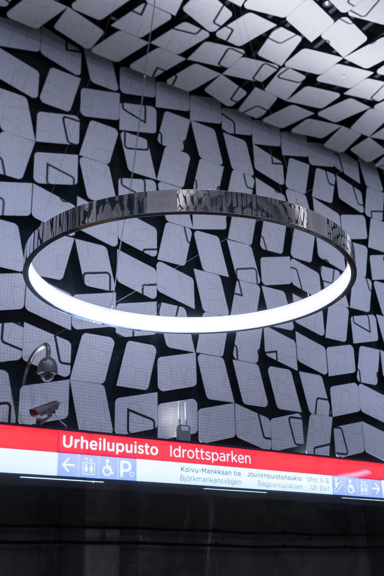 Grafische schwarz weiße Wand und Decke mit einer Aluminium polierten Ringleuchte (CIRCOLO) davor, die die Umgebung in sich spiegelt.