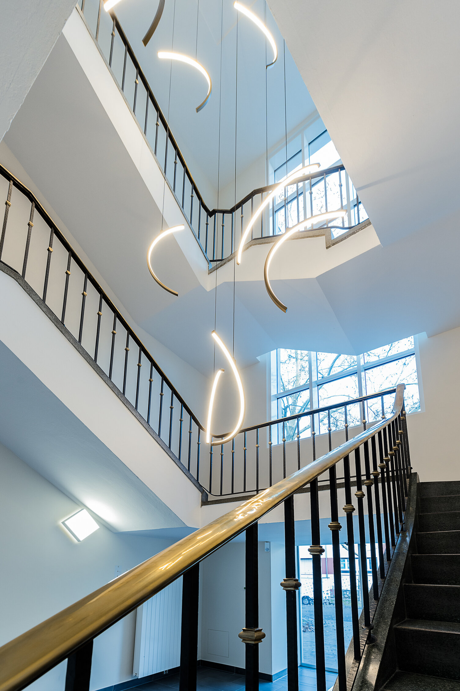 SLIM-Kreissegmente Lichtobjekt im Treppenhaus | © eydos GmbH Kronleuchter/ Lichtobjekt im Treppenauge eines Firmengebäudes der VCC Group, bestehend aus Kreis-Segmenten der SLIM Ringleuchten nach innen leuchtend und dem Leuchtenprofil aus Aluminium in gold. | © eydos GmbH