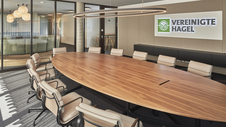 Meeting room with DOPPIO ELLIPSE light, oval wooden table, white chairs, and company logo on the wall. | © Norbert Miguletz Fotografie 