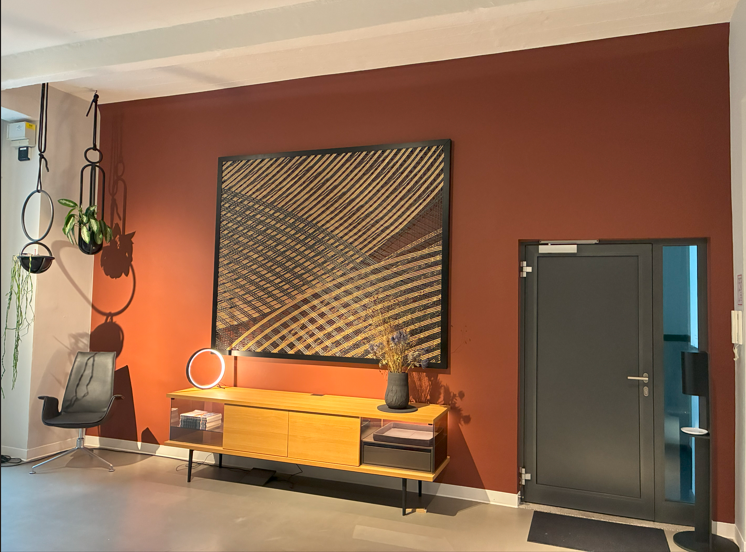 Ambientelicht - Runde dekorative Tischleuchte SLIM TABLE Rechts im Bild eine Tür, nach links eine rote Wand vor der eine Holzanrichte steht, auf dieser ist ein kleiner schwarzer vertikal aufgestellter Lichtring, SLIM TABLE. Darüber hängt ein grafisches Bild. Links im Eck ein Ledersessel von Walter Knoll.