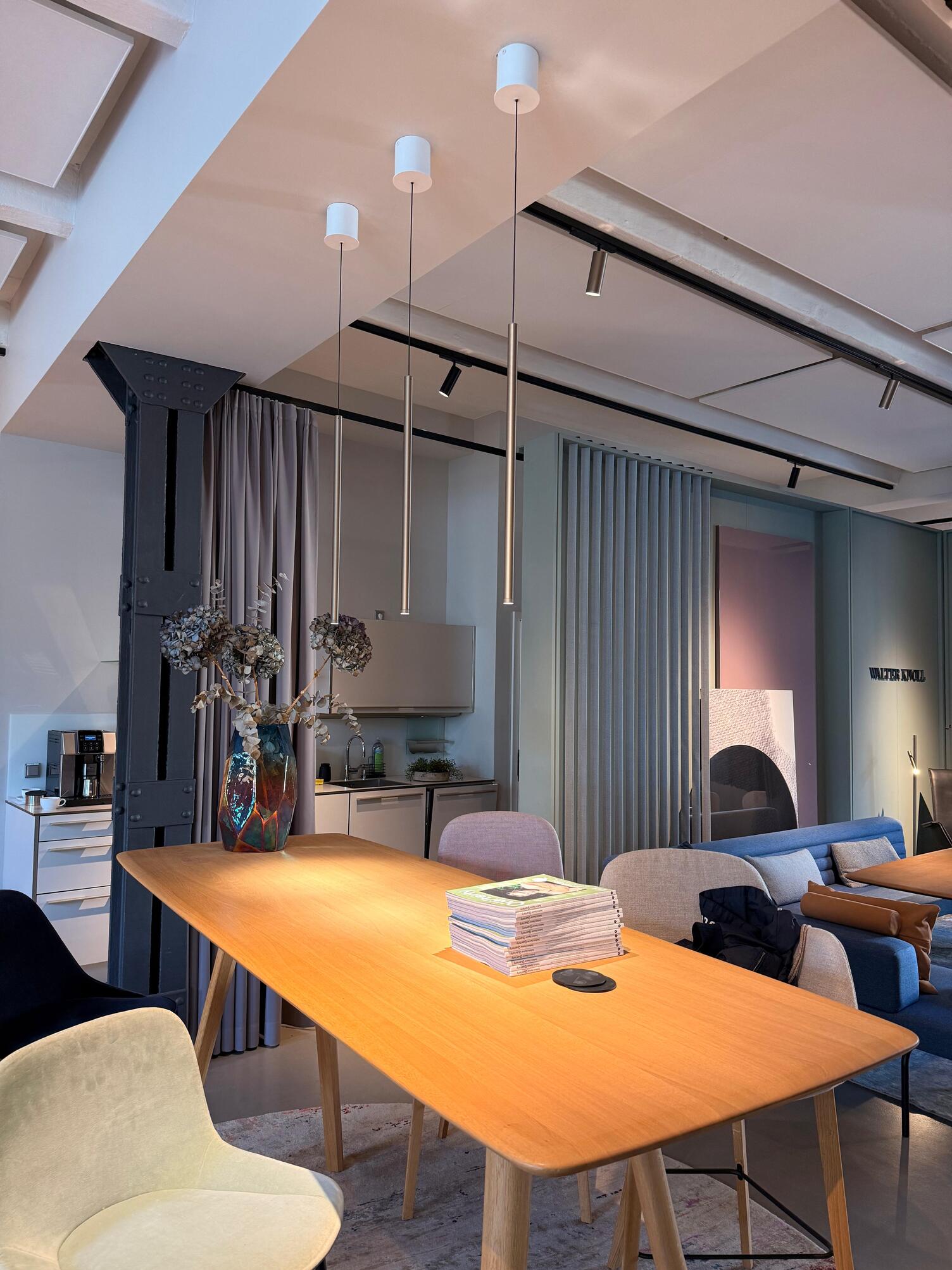  Brown wooden high table with bar stools. Three elegant cylindrical pendant lights from the FINO luminaire series by SATTLER are suspended along its length. 
