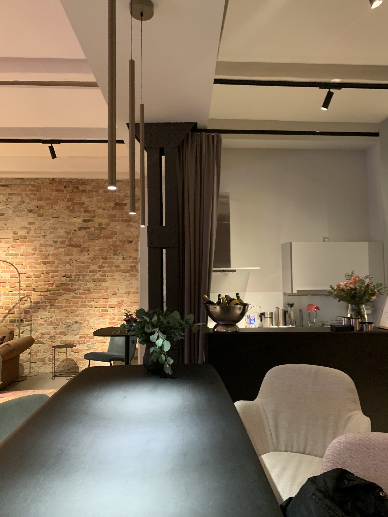 Stimmungsvolles elegantes Barlicht Schwarzer Bartisch von Walter Knoll mit 3 schmalen bronze-farbenen Stableuchten, Fino Pendant, entlang der Länge. Im Hintergrund Blick in eine kleine Küche.