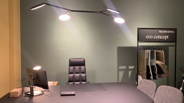 View of an individual workstation with a black table and leather armchair by Walter Knoll. On the table is a table lamp with a round, flat light head, AVVENI TABLE by SATTLER. Above the table is a branched black pendant lamp with four arms, each ending in a round, flat, movable light head.