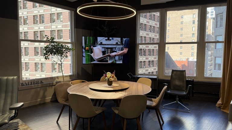 Essraum mit großen Fenstern und Blick auf den Broadway, in der Mitte ein runder Esstisch mit Stühlen aus Holz von Walter Knoll. Über dem Tisch hängt eine Ringleuchte von SATTLER der Serie DOPPIO, die den Tisch erleuchtet und einen runden Rahmen für die Essecke gestaltet.
