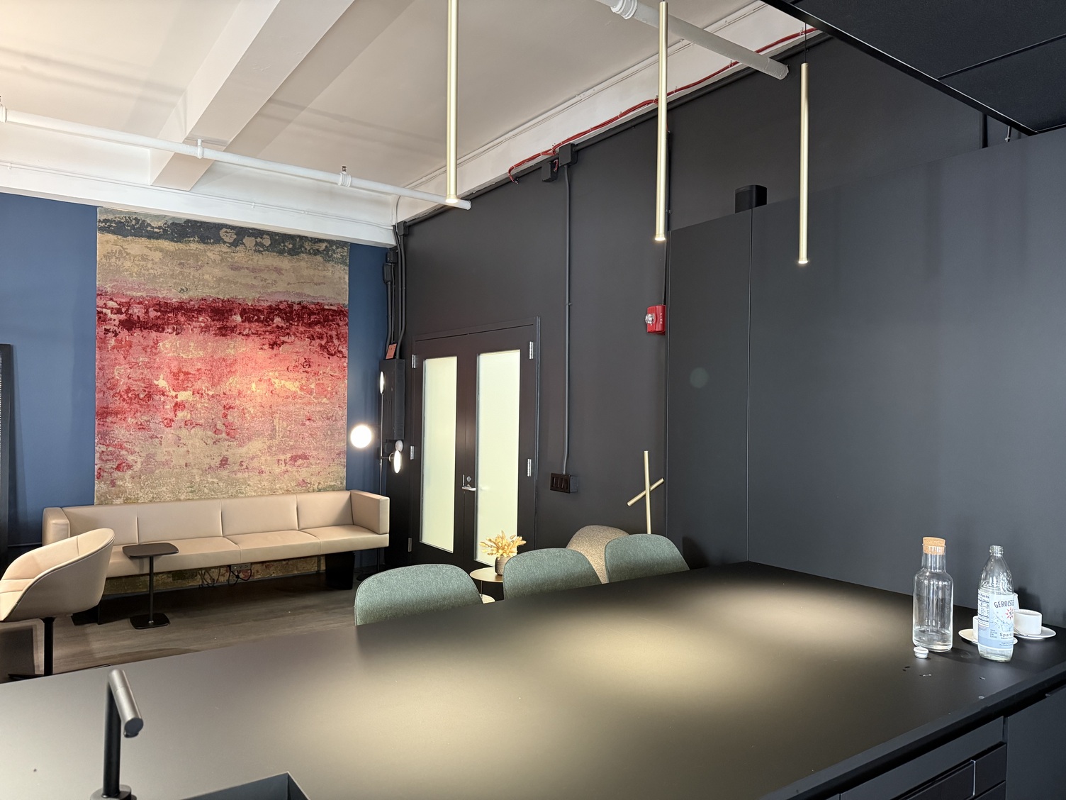 Theke mit Zylindrischen Hängelampen FINO PENDANT Schwarz-graue hohe Esstheke mit grünen gepolsterten Hochstühlen über der 3 dünne stabförmige champagner Goldene Pendelleuchten FINO PENDANT entlang der Länge pendeln.