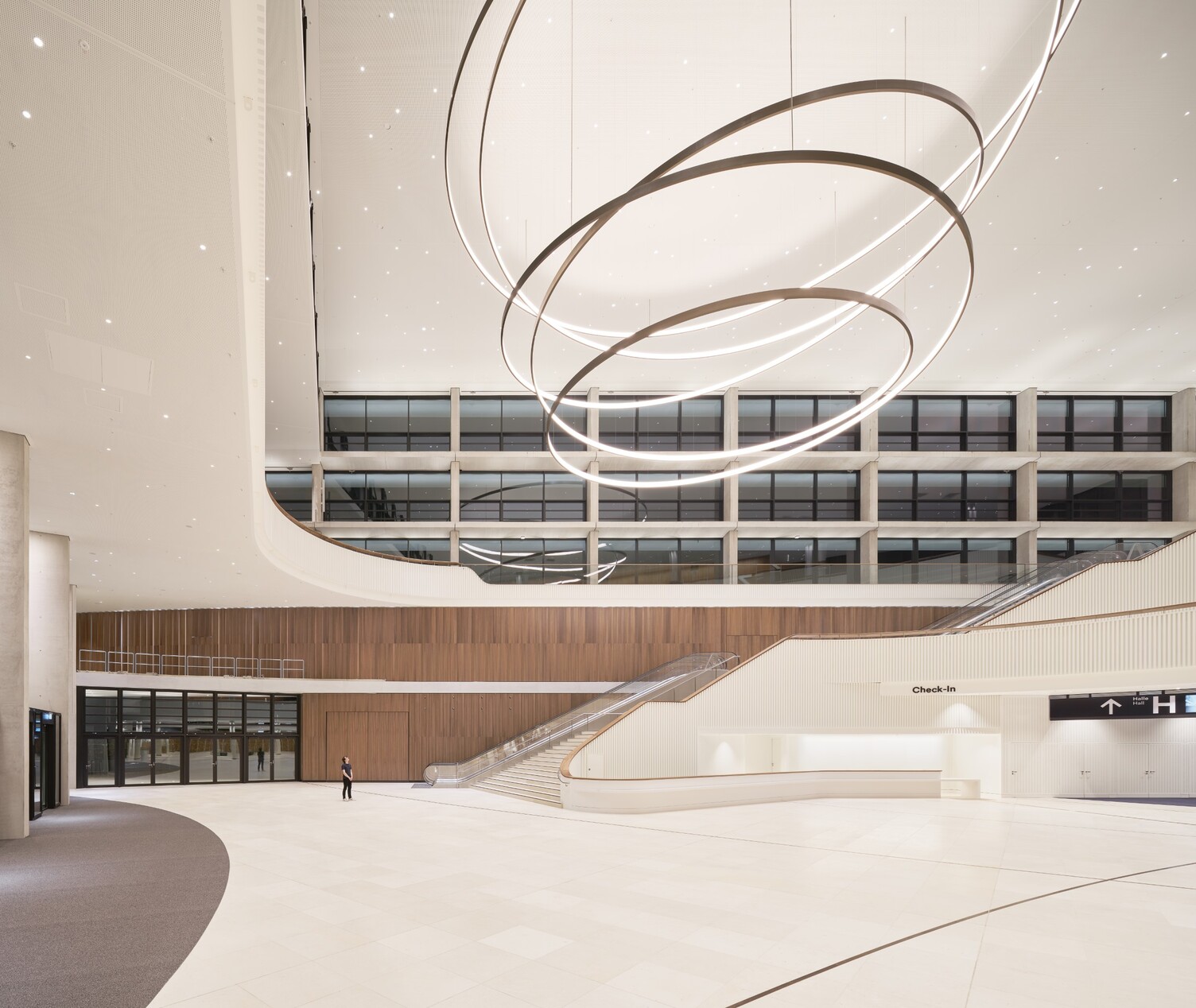 A person stands in the entrance area of the CCH Hamburg and looks up at a room-filling spiral luminaire.